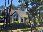 Classic Cape exterior with arched window and wooded setting, a peaceful Eastham vacation home arrival.