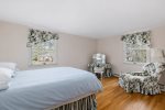 Spacious bedroom with comfortable bed, sitting chair, and sunny windows, classic Cape Cod comfort