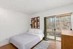 Simple bedroom with a queen bed and sliding door to the deck, offering wooded views and easy outdoor access.