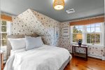 Another view of this inviting queen bedroom highlights the woven bed, warm wood floors, and cheerful Cape Cod style.