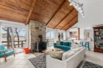 Sunlit great room at Marshside Escape with cathedral wood ceilings, stone fireplace, and sliding doors opening to South Wellfleet marsh views.
