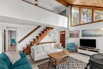 Bright Cape Cod living room with TV lounge seating, soaring windows, and staircase to the upper level twin bedrooms.