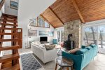 Another view of the airy living room, showcasing cathedral ceilings, wood stove warmth, and water views through oversized sliders.